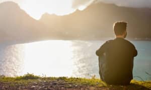 man sitting on the ground looking at a scenic view of a lake and mountains