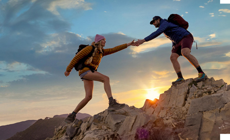 Two backpackers helping each other walk on rocks together