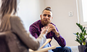 A man sitting with his hands together active listening to someone speak